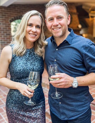Jason and his wife dressing up in a formal outfit taking photo while holding wine glasses